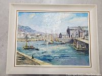 Front view of the framed vintage oil painting showing a harbor with dockside buildings, boats, and mountains in the background.