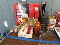 Full lot shown including Solaris whiskey decanter set in box, manual wine openers, electric wine opener, cocktail shakers, jigger, Miller vintage glasses and shot glasses on table.