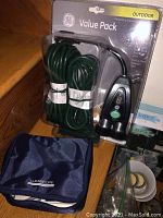 Photo showing coiled green extension cords and black digital timer device, in original GE Value Pack packaging. Blue Lumiscope carrying case is visible.