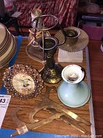Photo showing multiple candle holders of different materials (ceramic, metal, glass) plus brass-colored decorative flat pieces and a metal picture frame stand