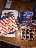 Photo of multiple music CDs including Michael Jackson The Ultimate Collection, 2004 Grammy Nominees, Junior soundtrack, and others stacked on hardwood floor.