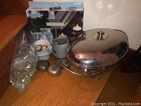 Photo showing the chaffing dish with lid and metal stand, LED tealight candles in packaging, metal weighted candle holders, and a plastic bag of clear beads on a wooden surface.