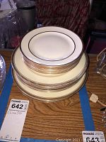 Stack of 6 Pope-Gosser saucer plates on top of larger Epiag plates showing gold rim and design