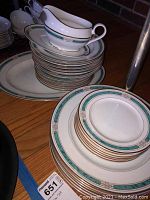 Photo showing stacks of dinner plates, bowls, and a gravy boat with matching green and gold design on white china.