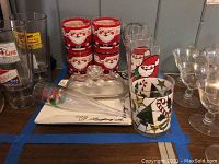 Photo showing four lowball Santa tumblers stacked, two highball Santa tumblers, Christmas tree wine glass, butter dish with lid, two plastic champagne flutes, and a Christmas plate.