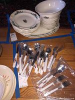 Dinner plates, salad bowl, bowls stacked together with serving platters and Christmas themed flatware grouped beneath.