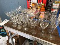Photo of three sets of cordial glasses and six single glasses on a metal table with blue wall background.