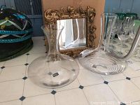 Two clear glass vases and a small framed mirror on a white tiled surface. The left vase has a Spiegelau label.
