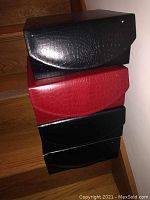 Stack of four leatherette jewelry boxes in black and red colors with croc-embossed texture, outside view