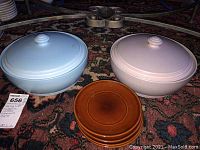 Two covered Pfaltzgraff stoneware casserole dishes in blue and pink with four brown plates in front.