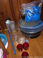 Multiple plastic platters stacked, clear plastic pitcher, 3 red tinted cups, multiple clear cups, plastic scoops in sealed bag, plastic liquid container.