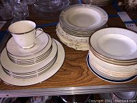 Set of Noritake china plates, saucers, and teacup with silver rims and embossed patterns, stacked and light dust visible