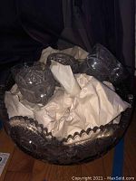 Glass punch bowl with scalloped edge and crumpled packing paper inside, surrounded by matching cups