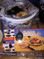 Hamilton Beach slow cooker wrapped in plastic with glass top and black utensils, sitting beside Mr. Pancake Gourmet Pancake Maker box