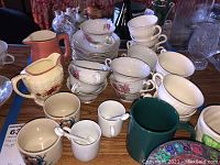 Overview of all items showing creamers, tea cups, saucers, mugs and spoons on tabletop.