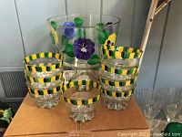Hand painted glass trifle dish with purple and yellow flower decoration, surrounded by eight small dessert bowls with green and yellow striped rims, all resting on a cardboard box.