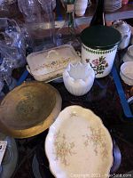 Overview photo showing various items: two white glass vases, floral-patterned tin container with wooden lid, floral Homer Laughlin platter, and large gold-toned shallow bowl