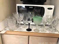 Photo showing 13 assorted wine glasses along with three heavy glass mugs of different styles and colors.