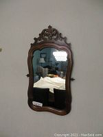 Front view of vintage solid wood mirror showing carved scroll detail at the top and beveled glass reflecting room.