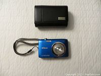 Top view of blue Nikon Coolpix camera front with case above it on white surface.