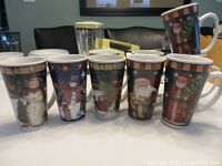 Nine large Christmas mugs standing upright showing festive snowman and Santa Claus holiday designs.