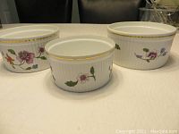 Three floral pattern Royal Worcester oval casserole dishes with ribbed texture and gold rims shown side by side on a white surface