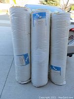 Three cylindrical rolls of wall insulation standing upright, wrapped in white plastic vapor barrier covering.