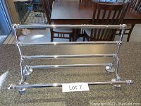 Front view of chrome train-style towel rack on countertop providing clear view of dimensions and design with horizontal bars and circular base feet.