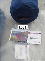 Photo of a blue cylindrical carrying sack with Therm-A-Rest logo and accompanying warranty and repair pamphlet, with label Lot 2 visible.