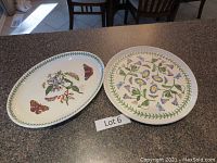 Two ceramic platters, oval with butterflies and round with floral design, on countertop.