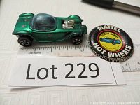 Vintage green Hot Wheels Red Line car, called Beatnik Bandit, alongside a badge with Mattel Hot Wheels branding. Car measures about 2.5 inches. Signs of light wear, clear bubble canopy, chrome engine detail, and red line tires.