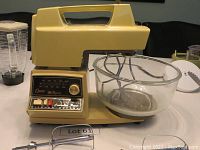 Photo of cream-colored Oster Regency stand mixer with glass mixing bowl and two beaters on table.