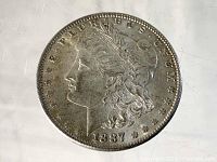 Obverse side of 1887 Morgan Silver Dollar coin showing Lady Liberty profile and date.
