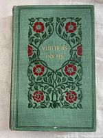 Front cover of the green cloth hardcover book with floral design and gilded title 'Whittier's Poems'.