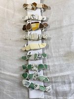 Front view of 9 sea pottery barrettes laid on white card, stones are varied colors of green, brown, yellow and white with decorative glaze