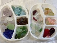 Top view of two white divided trays filled with various pieces of sea glass sorted by color including green, blue, brown, purple, pink, red, yellow, and clear.