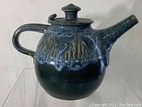 Side view of blue stoneware teapot showing handle, spout, textured decoration and lid.