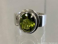 Close-up front view of chunky sterling silver ring with oval faceted green peridot stone.