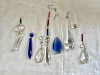 Eight assorted crystal sun catchers laid out on a white background, showing various shapes and colors including clear and deep blue crystals, some with red and green bead accents. Loop strings attached for hanging.