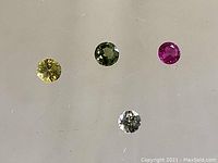 Four faceted sapphires in yellow, green, pink, and light blue/clear are displayed on a reflective surface.