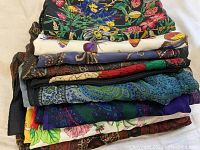 Stack of nine folded scarves showing various colorful patterns including floral and butterfly designs.
