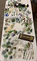 Wide view of the table covered with various sea glass items including sculptures, jewelry, candle holders, and small decorative pieces arranged in groups.