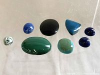 Top-down view of all polished cabochon stones laid out on clear surface, showing size, shape, and color variety