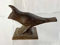 Angled view of the dark brown hand-carved wooden bird sculpture showing crest, detailed wing feathers, and square base.