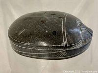 Top angled view showing the smooth, dark stone scarab paperweight with engraved lines defining the scarab's wings and head.