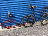 Full lot showing red Nineteen frame and black Pinarello frame with wheels against blue storage door