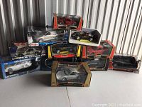 Group photo of ten Burago and Maisto new model cars in original packaging, various sports and classic car models visible; packaging shows some wear and creases from display.