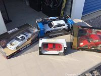 Four model cars in original packaging displayed on outdoor table, including various brands.