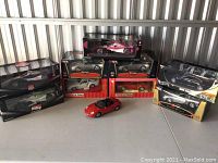 View of multiple Burago Plus model cars with boxes and one unboxed red convertible.
