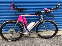 Full left-side view of the bike against a blue backdrop showing frame, wheels, aerobars and accessories